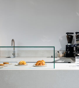 Spot Café Ein Cafe-Tresen mit Kaffeemaschinen, Spüle, Tellern mit Crossaints und Zimtschnecken.